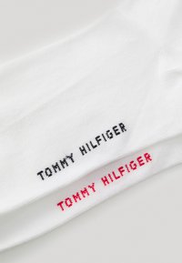 Weiße Baumwollsocken mit dem Logo "TOMMY HILFIGER" in schwarster und roter Stickerei. Der Text ist entlang des Bündchens positioniert und hat eine gerippte Struktur.