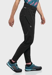 Schwarze Outdoor-Hosen mit schlanker Passform, ausgestattet mit einer Reißverschlusstasche und reflektierenden Akzenten. Hergestellt aus robustem, leichtem Material.