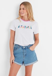 White cotton t-shirt with multicolored floral "ALOHA" text, featuring a pink ribbed collar, paired with high-waisted blue denim shorts.