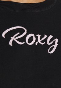 Felpa nera con un evidente logo "Roxy" ricamato in rosa in un carattere corsivo. Tessuto liscio con un collo a costine.