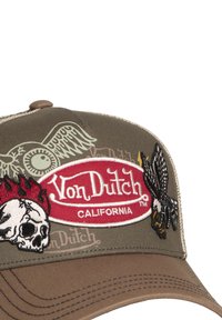 Gorra de béisbol color caqui con detalles bordados: calavera, águila y alas. Presenta un parche de logo rojo con la inscripción "Von Dutch California." Tejido texturizado.