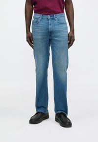 Svetlomodré džínsové nohavice s rovnými nohavicami, v štýle s piatimi vreckami a jemným vyblednutím. Majú klasické zapínanie na gombík a zips.