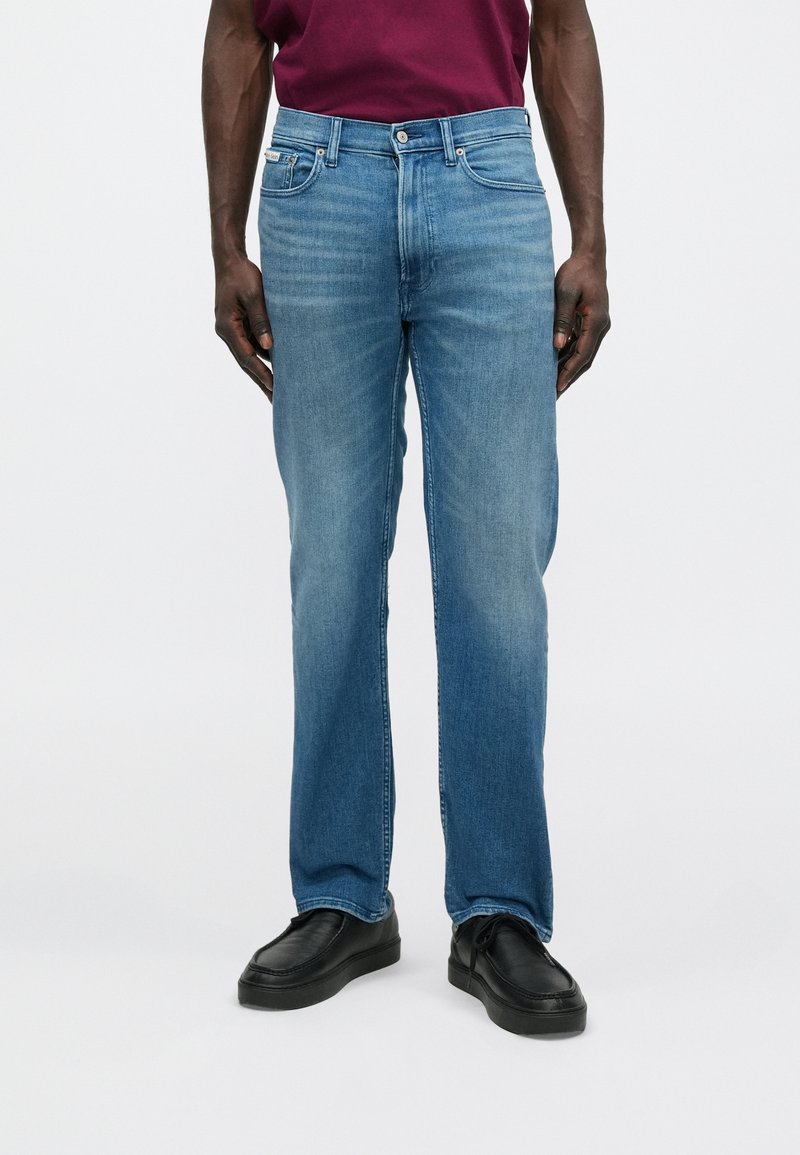 Svetlomodré džínsové nohavice s rovnými nohavicami, v štýle s piatimi vreckami a jemným vyblednutím. Majú klasické zapínanie na gombík a zips.