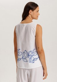 Top sin mangas blanco con bordado floral azul en el dobladillo. Tela suave y ligera con un corte relajado. Escote redondo en la parte posterior.