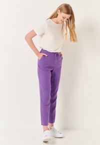 Paarse linnen broek met een taps toelopende pasvorm, een koordsluiting in de taille en zijzakken, gecombineerd met een effen wit T-shirt met korte mouwen en witte sneakers.