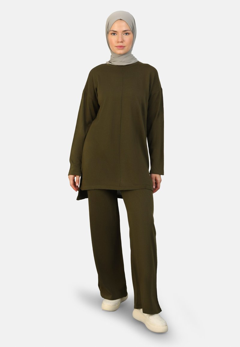 Olive green knit tunic and pants set with long sleeves. Textured fabric, loose fit, and side slits. Paired with white sneakers.