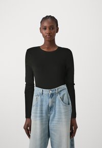 Zwarte langekous top met een ronde hals, gecombineerd met lichtblauwe, loszittende denim jeans. Heeft een gladde textuur en een ontspannen ontwerp.