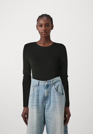 Black long-sleeve top with a round neck paired with light blue, loose-fitting denim jeans. Features a smooth texture and relaxed design.