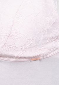 Bustier u mekom ružičastom s cvjetnim čipkastim prekrivačem, s glatkim elastičnim donjim slojem i malim oznakom na donjoj ivici.