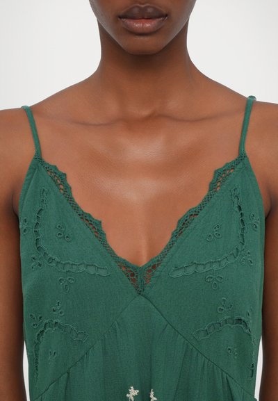 Πράσινο αμάνικο φόρεμα με βαθύ V-ντεκολτέ, διακοσμημένο με κεντημένα λουλουδένια μοτίβα και λεπτή δαντέλα στις ώμους και τον λαιμό.
