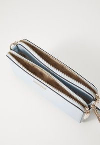 Světlá modrá peněženka na zip se dvěma přihrádkami, s hladkým vnějškem a vzorovanou vnitřní podšívkou. Stříbrné kovové doplňky.