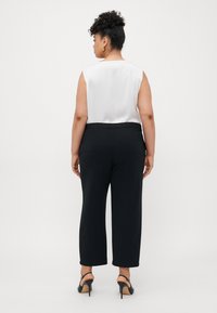 White sleeveless blouse with smooth texture, paired with black wide-leg trousers and black heels; viewed from the back.
