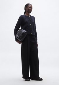 Μπλε σκούφο πλεκτό cardigan με χρυσά κουμπιά, σε συνδυασμό με μαύρο παντελόνι με φαρδιά πόδια και ψηλή μέση και μαύρη δερμάτινη τσάντα, τοποθετημένα σε απλό φόντο.