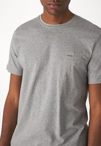 Γκρι κοντομάνικο μπλουζάκι από μείγμα βαμβακιού, με μικρή τετράγωνη λογότυπη ετικέτα στην αριστερή πλευρά του στήθους. Λείο υφή και κλασική εφαρμογή.