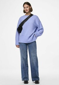 Lavendelkleurige oversized gebreide trui met geribde boorden en onderrand, gecombineerd met high-waisted jeans met een ruwe zoom en een zwarte schoudertas.