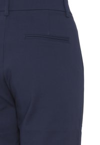 Gros plan sur l'arrière d'un pantalon bleu marine ajusté avec une poche passepoilée horizontale unique et des passants de ceinture.