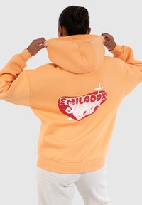 Sweatshirt à capuche orange avec une poche kangourou, présentant un grand logo graphique rouge et blanc au dos, fabriqué en tissu en mélange de coton doux.