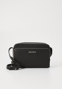 Black leather crossbody bag with two zippered compartments, embossed logo, and an adjustable strap. Features a textured finish.