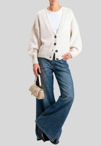 Cardigan lavorato a maglia color bianco sporco con scollo a V, vestibilità oversize, cinque bottoni neri e orlo a coste. Abbinato a jeans a zampa d'elefante blu e una piccola borsa beige.