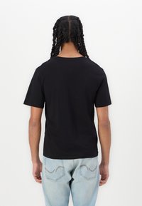 Zwarte katoenen t-shirt met korte mouwen, ronde hals en een relaxte pasvorm, gecombineerd met lichtblauwe jeans met gestikte zakdetails.
