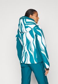 Sinine puffer-jakk, millel on valged ja rohelised abstraktsed triibud, koos kapuutsiga, vatitekkide tekstuuriga ja elastsete mansettidega. Kitsas siluett koos taskutega.