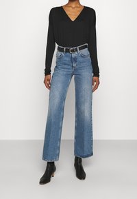 Haut noir à manches longues et décolleté en V associé à un jean large taille haute bleu clair. Ceinture noire avec boucle rectangulaire et bottines noires.
