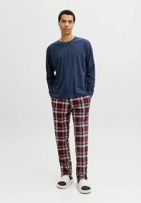 Haut à manches longues bleu marine, pantalon à carreaux avec des accents rouges, bleus et blancs, et chaussures légères à enfiler. Tenue décontractée pour se détendre.
