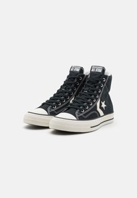 Zapatillas altas negras con puntera de goma blanca, suela texturizada, costuras blancas y parche con logo en la lengüeta. Fabricadas en material de lona.