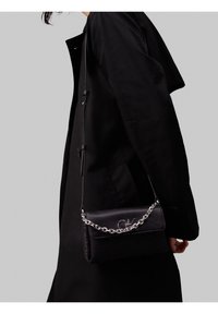 Borsa nera in ecopelle con tracolla a catena, caratterizzata da un motivo testurizzato e un dettaglio logo argentato sulla parte anteriore. Forma rettangolare.