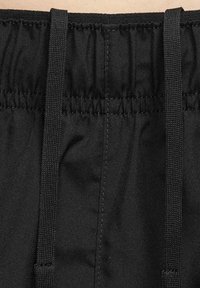 Czarna elastyczna talia z marszczoną fakturą i sznurkami do zaciągania. Tkanina wygląda na gładką, o matowym wykończeniu. Brak dodatkowych wzorów czy detali.