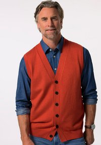 Oranžový bezrukávový svetr s výstřihem do V, knoflíkovým zapínáním a žebrovaným lemem, přeložený přes džínovou košili s knoflíkovými manžetami.