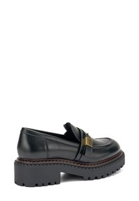 Mocassini in pelle nera con suola chunky, cinturino decorativo con un accento dorato e dettagli cuciti lungo i bordi. Modello di battistrada resistente.