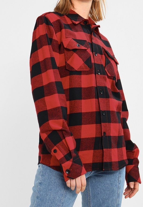Chemise en flanelle à carreaux rouges et noirs avec poches poitrine boutonnées et boutons noirs portée avec un jean bleu clair.