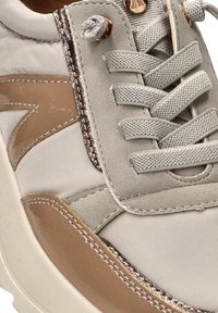 Zapatillas beige y crema que presentan una mezcla de materiales lisos y texturizados, diseño de cordones y detalles en bronce.