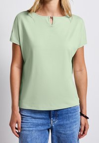 Ljusgrön kortärmad topp med rund halsringning som har en liten nyckelhålsöppning och silverdetaljer. Mjuk och slät tyg.