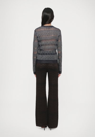 Ilgomis rankovėmis, pusiau permatomas tamsiai mėlynas mezginys su zigzago raštais, derinamas su aukšto liemens, plačiomis juodomis kelnėmis.