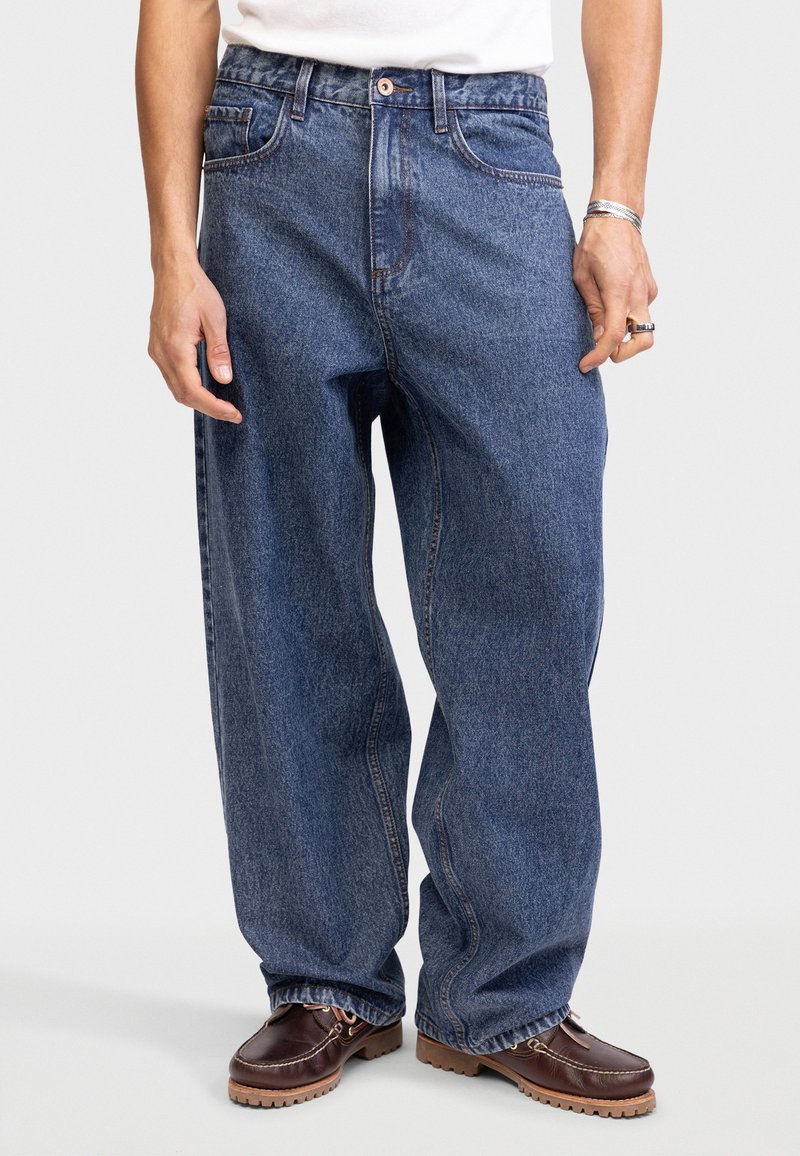 Blauwe denim jeans met een loose fit, voorzien van voorkruiszakken en een knoop in de tailleband. De textuur is iets vervaagd met een klassiek ontwerp.