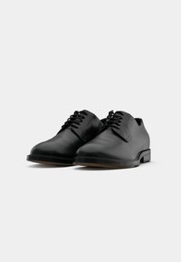 Scarpe eleganti in pelle nera con punte arrotondate, lacci piatti e un design minimalista. Suola in gomma e texture liscia.
