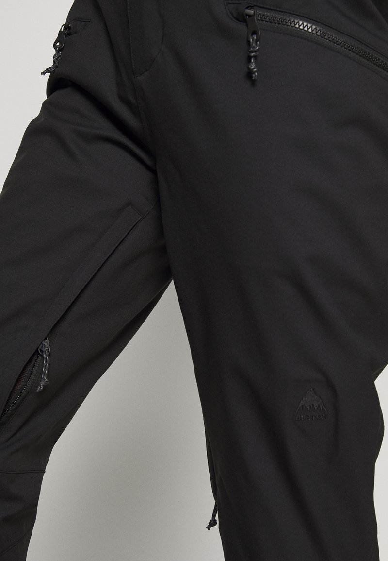 Schwarze Outdoor-Hosen mit Reißverschlusstaschen, aus einem glatten, dehnbaren Stoff. Mit einem subtil geprägten Logo und verstellbaren Kordelzugverschlüssen.