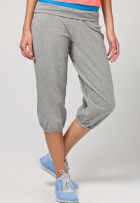 Pantaloni capri grigi realizzati in un tessuto morbido, con vita elasticizzata e polsini arricciati. Abbinati a scarpe da ginnastica azzurre.
