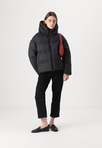 Zwarte pufferjack met een capuchon, voorzien van horizontale stiksels en een rits aan de voorkant. Gepaarde met zwarte cropped broeken en zwarte loafers, met een rode tas.