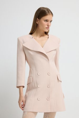 Jasnoróżowy podwójny płaszcz z szerokimi klapami, wyraźnie zarysowanymi ramionami i dwiema przednimi kieszeniami. Gładka tekstura i dopasowany krój.