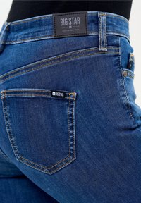 Jeans de mezclilla azul oscuro con un corte estructurado, sutil desgaste, costuras amarillas y una etiqueta negra de "BIG STAR" en la cintura.