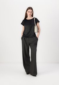 Zwarte satijnen top met korte mouwen, gecombineerd met hoge taille, wijd uitlopende gestreepte broek, aangevuld met een kleine, lichte handtas.