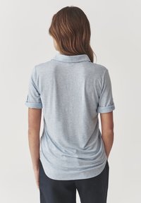Light blue polo shirt made of soft fabric, featuring a collar and rolled sleeves. The back shows a curved hem and smooth texture.
