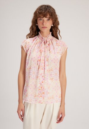 Bloes met bloemenprint in lichte stof, met een ruches-kraag, korte mouwen en een roze en oranje patroon met ingewikkelde bloemontwerpen.