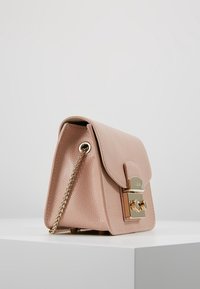 Piccola borsa a tracolla in pelle texture rosa chiaro con catena dorata e chiusura a lucchetto dorata, esposta su una superficie bianca contro uno sfondo grigio.