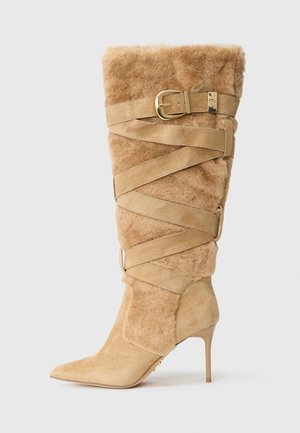 Knee-high bež semiš stiletto čizma s šiljastim nožnim prstom, pahuljastom teksturom od krzna i preklapajućim trakama s zlatnom kopčom sa strane.