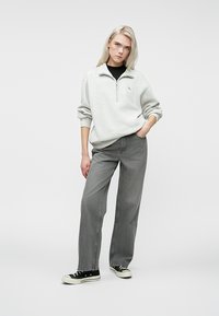Sweatshirt zippé gris clair avec un col haut, associé à un pantalon large gris foncé et des baskets noires. Tenue propre et décontractée.