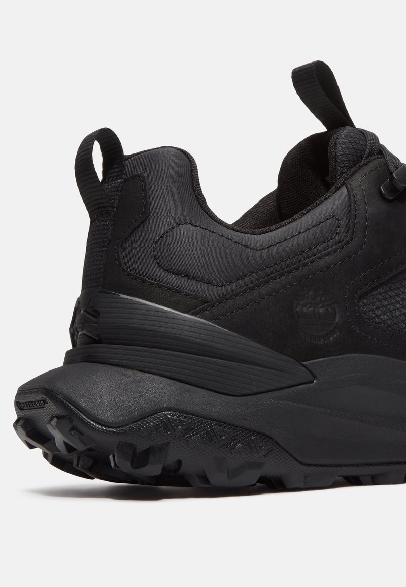 Zapatilla deportiva negra con un upper texturizado, talón reforzado y suela resistente con tacos prominentes para mayor agarre. Incluye una cinta de tirón para facilitar el uso.